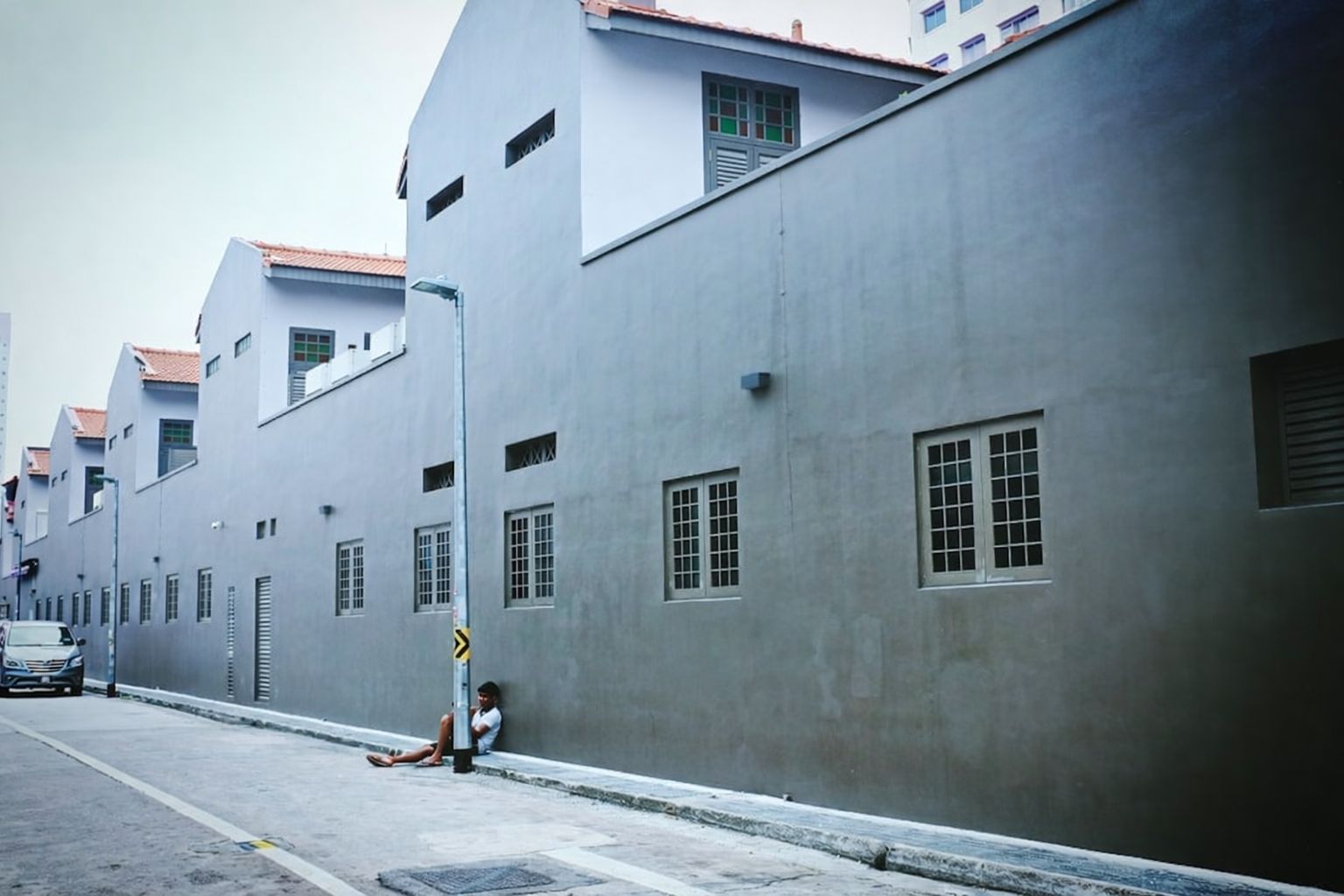 Lång rad av hus med grå fasader och en man som sitter på trottoarkanten.