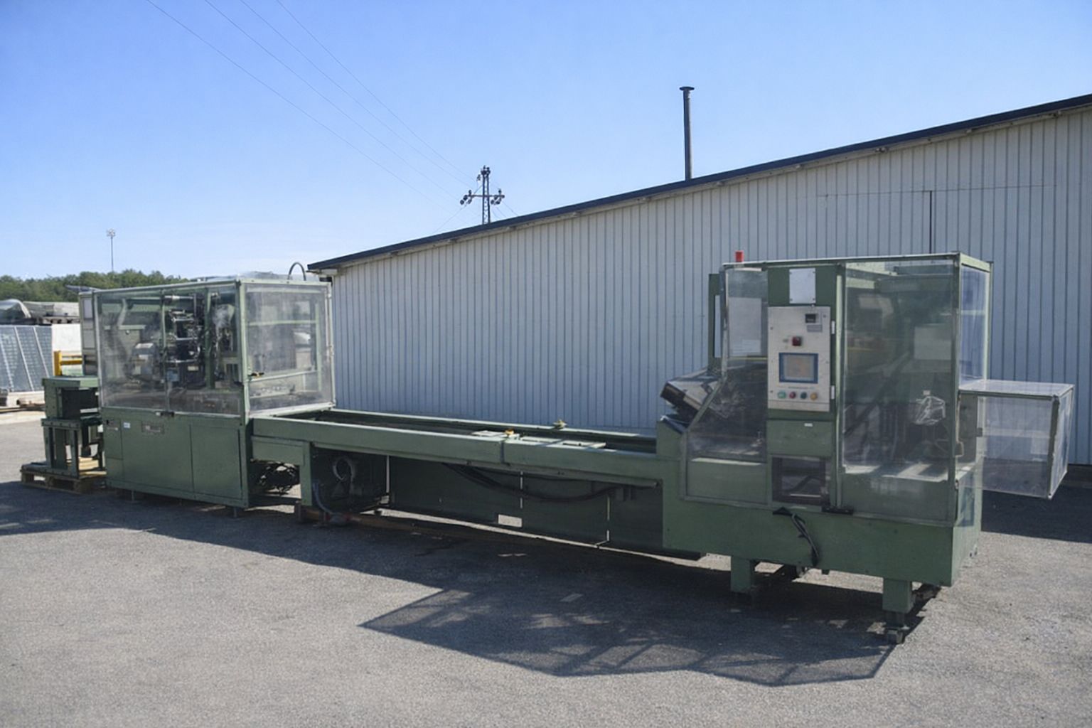 Lång, grön industrimaskin med transparenta skydd, utomhus vid byggnad